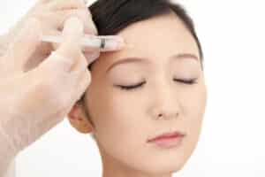 Medical provider injects Botox in a young woman's forehead lines