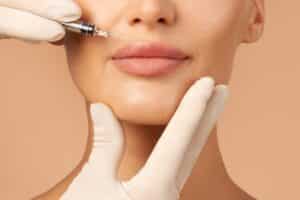 Woman smiles slightly as a doctor injects a dermal filler in her lips