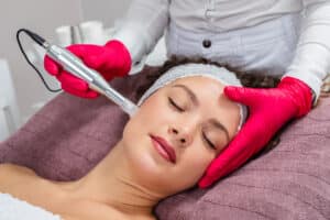 Woman with dark hair, wearing a white spa headband, closes her eyes during a PRP treatment for facial volume